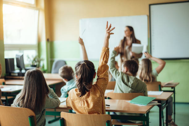 Classroom with students raising their hands to ask questions during a lesson.