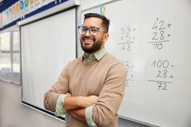 A teacher explaining a math lesson by writing equations on a whiteboard.